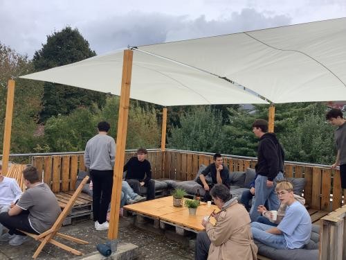 Einige handwerklich begabte Schüler, die mittlerweile die 10. Klasse besuchen, nahmen sich gemeinsam mit ihrer Klassenlehrerin Victoria Bansemer einer Dachterrasse an der Hebelschule in Schliengen an und schufen einen Rückzugsort zum Entspannen. Schüler sitzen auf den selbst gebauten Palettenmöbeln auf der Dachterrasse