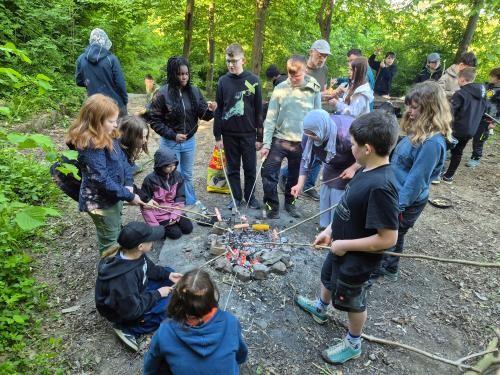 Schülergruppe grillt im Wald über offenem Feuer.